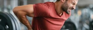 A man at the gym winces and holds his back as he experience several types of back pain