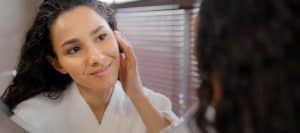 A woman smiles and touches her face as she looks in a mirror after platelet rich plasma facial treatment
