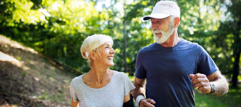 An older couple smiles as they jog