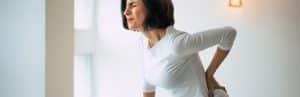 A woman winces and holds her lower back due to one of the types of back pain