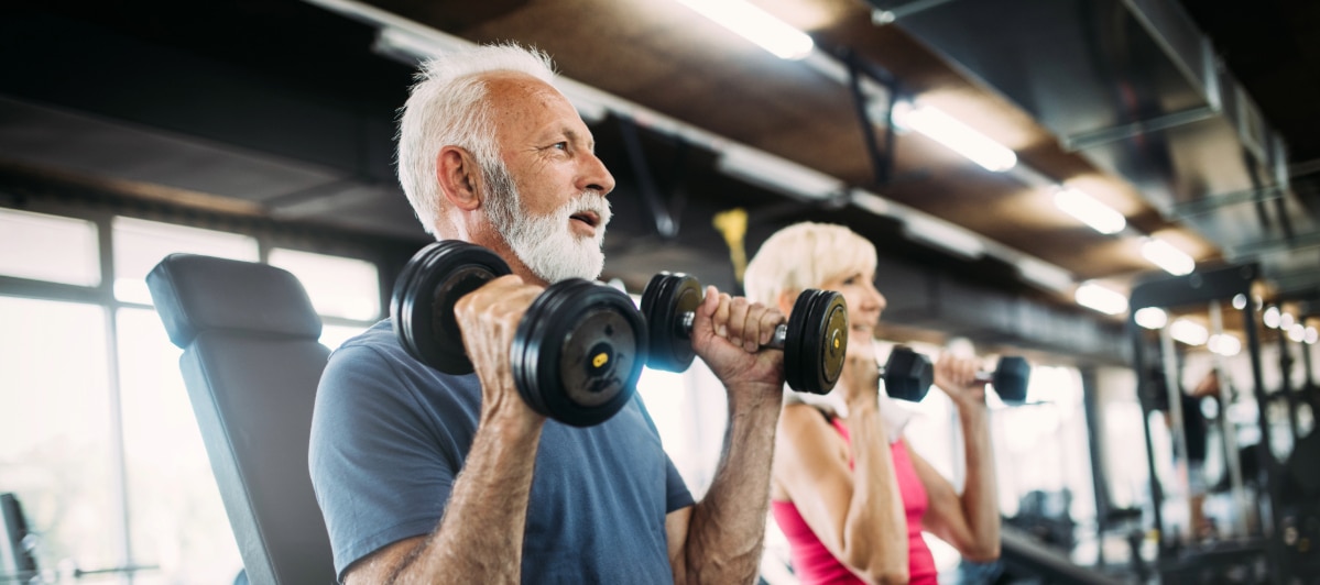 A Guide to Chronic Pelvic Pain Causes and Treatments-6-Gym An older couple smile as they lift weights in a gym after treatment for chronic pelvic pain
