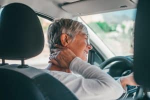 Rear view of old woman having neck pain while driving a car