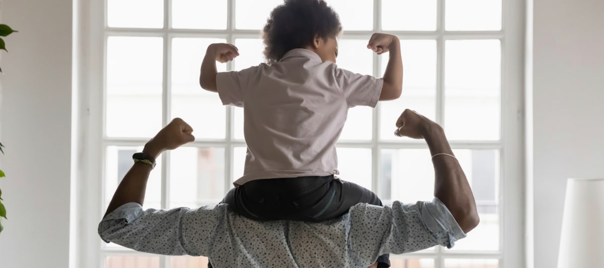 A dad with his son on his shoulders both flex their arms to demonstrate strong back strength