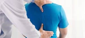 A back pain specialists evaluating a male patient in a blue shirt.