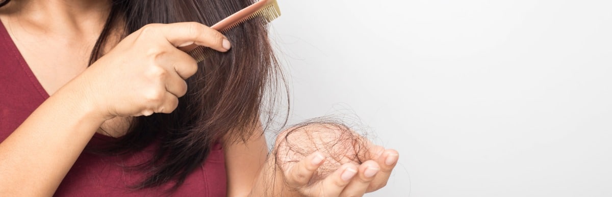 A woman holds loose strands due to hair loss as she uses a comb