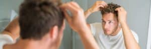 A man looks in the mirror and checks his scalp for hair loss