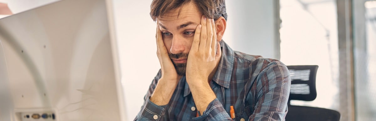 Can Hormone Replacement Help Hair Loss-4 A man sitting at an office desk puts his hands to his face from fatigue due to hair loss