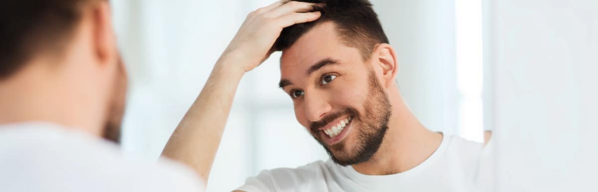 Can Hormone Replacement Help Hair Loss-6 A man smiles as he checks for hair loss in the mirror