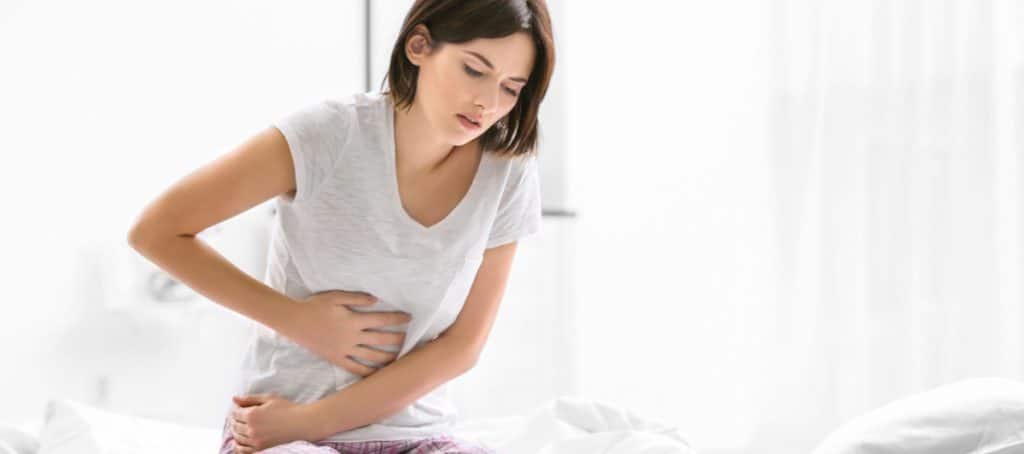 A woman sits on her bed and holds her stomach from abdominal pain from diabetic neuropathy