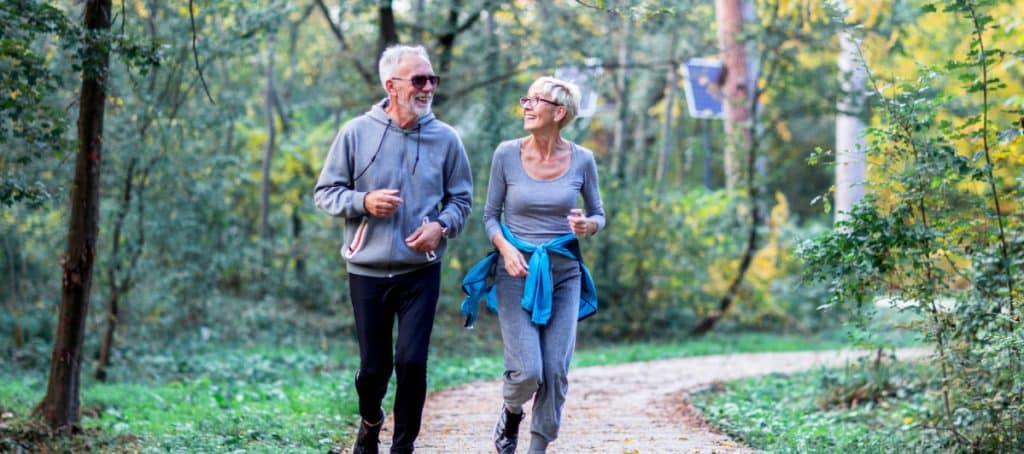 An older couple smiles at each other as they jog on a nature trail to mitigate the effects of diabetic neuropathy