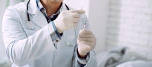 A doctor in a lab coat holds a needle as he prepares to administer trigger injections