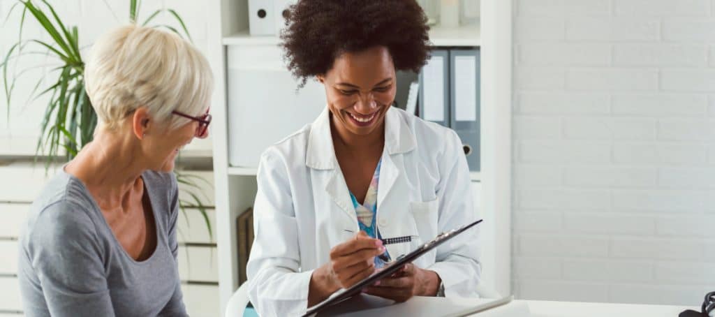 A doctor smiles as she goes over a clipboard about the signs and symptoms of diabetic peripheral neuropathy with a patient