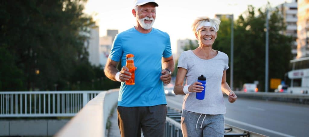 An older couple smiles as they walk briskly for exercise while holding water bottles