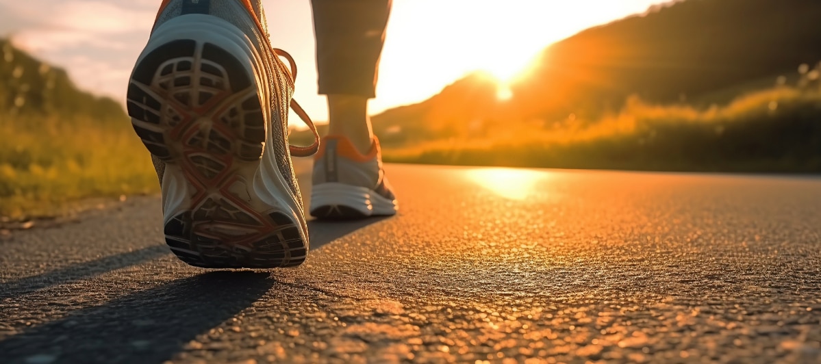 An image of a person with running shoes on walking on a trail towards a sunset