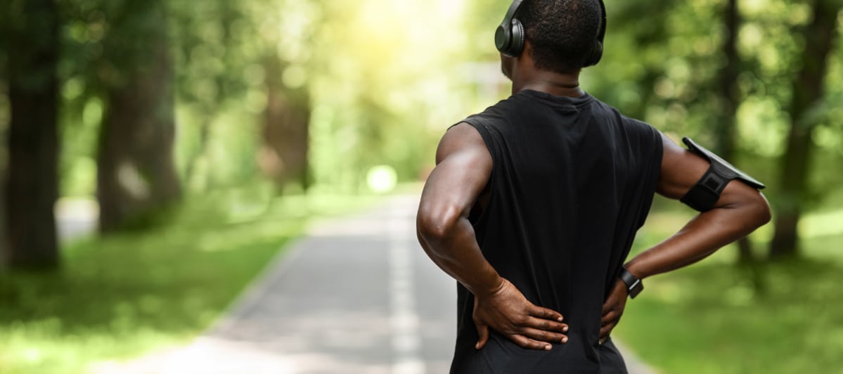 Explore 5 Symptoms of Middle Back Pain-2-Runner A runner stands on a nature trail and holds his back due to middle back pain
