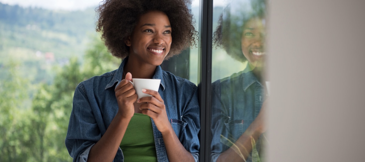 Exploring Stellate Ganglion Block Injections for Complex PTSD-4-Smiling Person A woman holds a cup of coffee and smiles due to stellate gangliong block injections for complex PTSD as she looks out a window