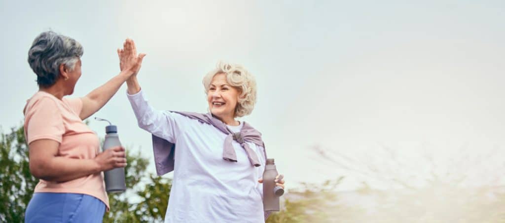 Two seniors high five as they take a walk in the park