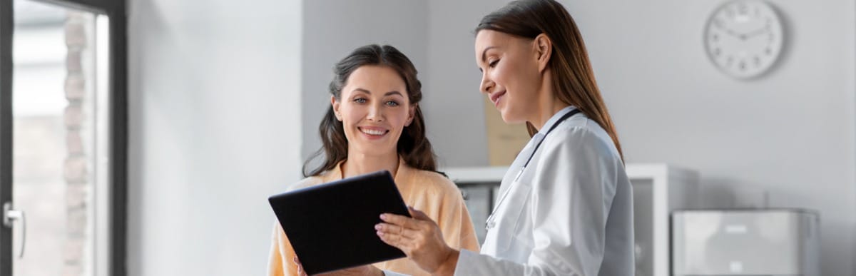 Four Benefits of a Diabetes Management Plan-2 A doctor in a lab coat points to a tablet and discusses a diabetes management plan with her patient