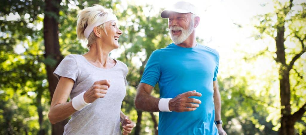 An older couple smiles at each other as they power walk on a nature trail due to diabetic neuropathy reversal