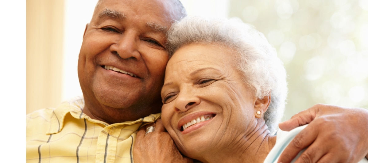 An older couple smiles as the man puts his hand around the woman