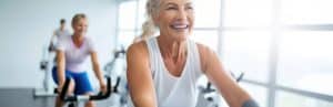A woman smiles and pedals during an exercise class with increased energy after Emsculpt Neo treatments