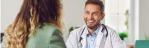 A doctor in a lab coat smiles while telling a patient about Emsculpt Neo treatment