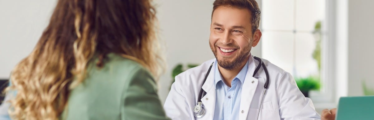 Heart Disease Symptoms You Need to Know (21) A doctor in a lab coat smiles as he tells a patient about injections to ease upper middle back pain