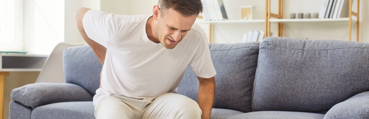 Heart Disease Symptoms You Need to Know (26) A man sitting on a couch holds his back due to herniated disc pain