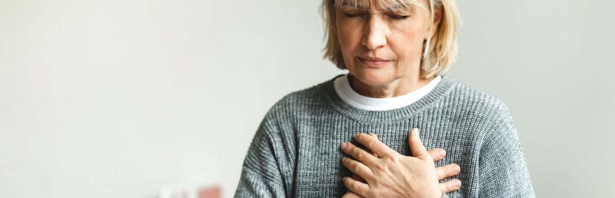 Heart Disease Symptoms You Need to Know (27) A woman puts her hands over her heart due to chest pain and upper back pain