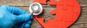 A doctor holds a stethoscope to a puzzle of a heart missing a piece