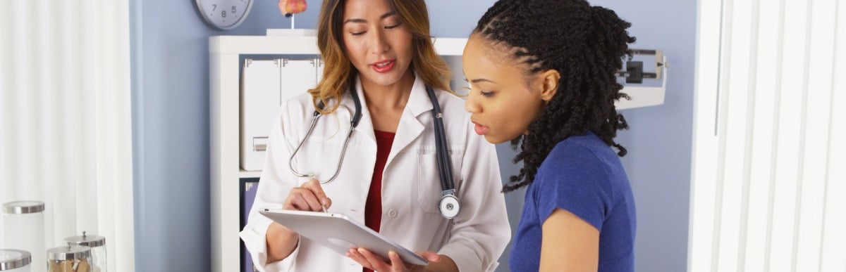 Heart Disease Symptoms You Need to Know (34) A doctor in a lab coat uses a tablet to discuss lumbar epidural injections with a patient