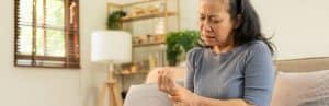 A woman sits on a couch and experiences pain in her hands which is one of the early signs of autoimmune arthritis