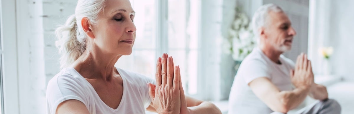 Heart Disease Symptoms You Need to Know (44) An older couple sit cross-legged and meditate to ease early signs of automimmune arthritis