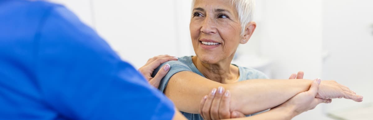 Heart Disease Symptoms You Need to Know (46) A woman smiles as a physical therapist helps her with shoulder flexibility to avoid the early signs of autoimmune arthritis