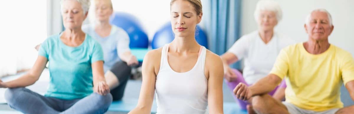 Heart Disease Symptoms You Need to Know (5) People in a yoga class sit cross-legged and meditate to reduce heart disease risk factors