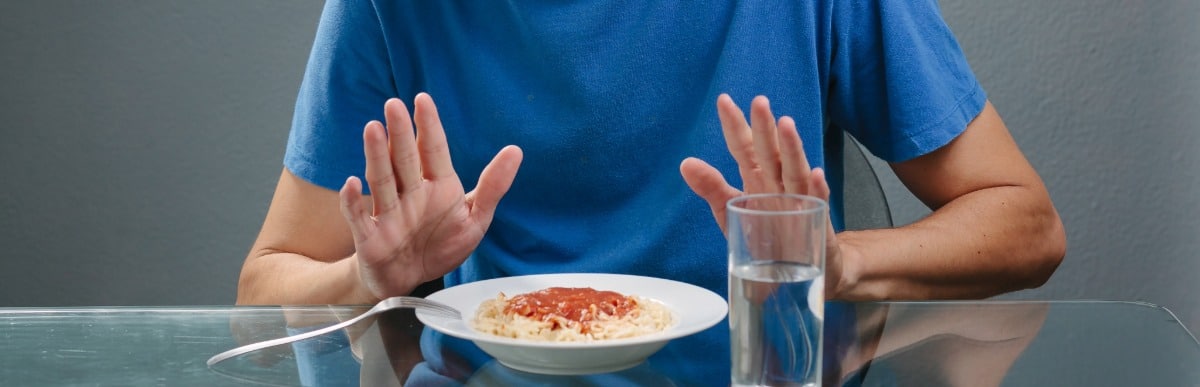 Heart Disease Symptoms You Need to Know (52) A man experiencing loss of appetite as one of the early signs of autoimmune arthritis pushes away a plate of spaghetti