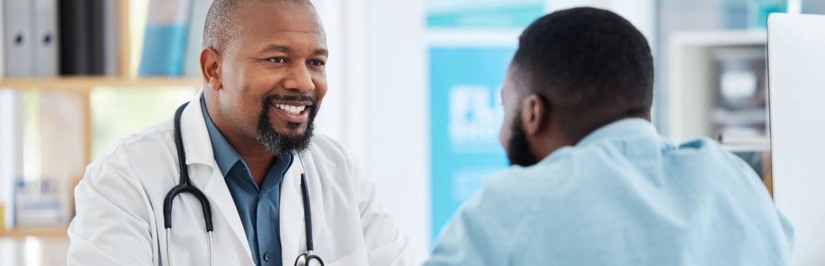 Heart Disease Symptoms You Need to Know (53) A doctor in a lab coat smiles as he talks to a patient about the early signs of autoimmune arthritis