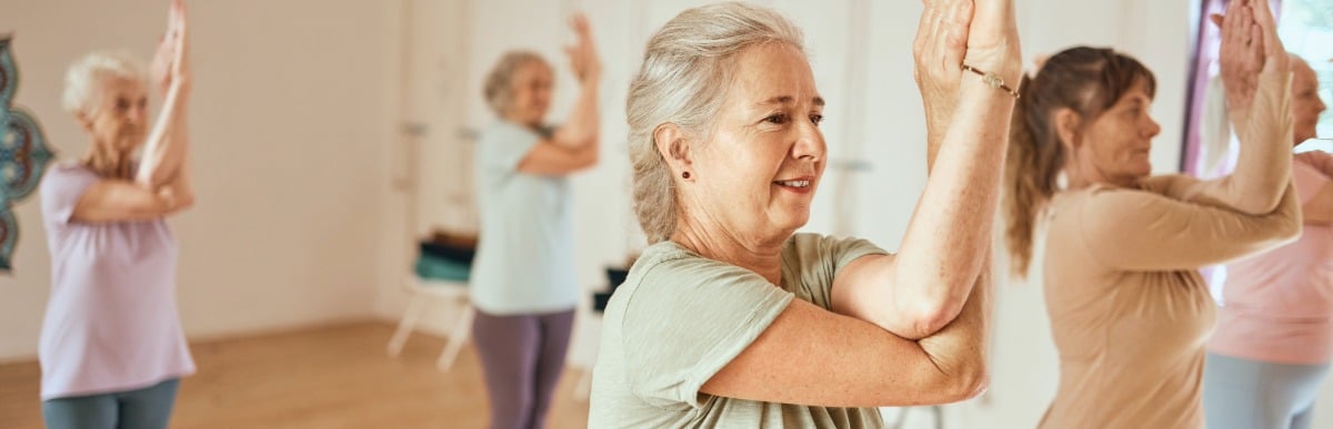 Heart Disease Symptoms You Need to Know (54) A woman smiles as she holds a pose with her arms during a yoga class