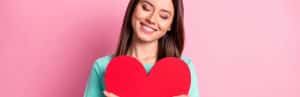 A woman hugs a large red paper heart to represent awareness of heart disease risk factors