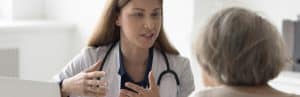A doctor in a lab coat tells a patient about kyphoplasty vs vertebroplasty