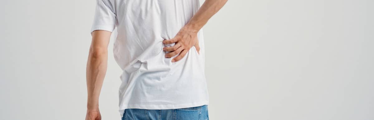 A man holds his back in pain as he thinks about his options: kyphoplasty vs vertebroplasty