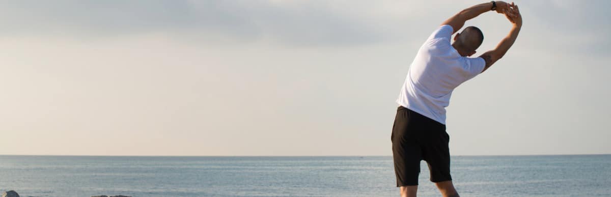 Heart Disease Symptoms You Need to Know (74) A runner stretches his back while standing on a beach as part of his vertebral compression fracture treatments