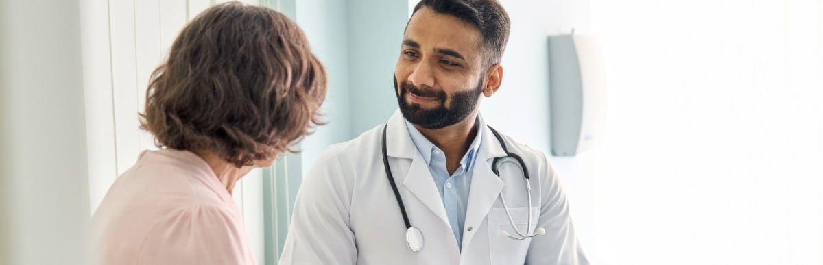 Heart Disease Symptoms You Need to Know (81) A doctor in a lab coat smiles as he listens to a patient ask about kyphoplasty recovery time
