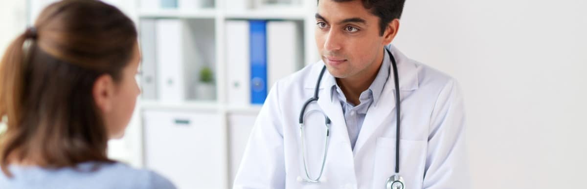 Heart Disease Symptoms You Need to Know (9) A doctor in a lab coat listens to a patient talk about finding middle back pain relief