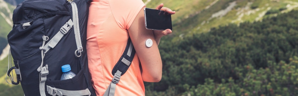 How Diabetes Management Programs Revolutionize Care-5 A backpacker checks her glucose monitoring device while on a hike
