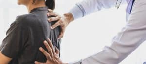 A doctor puts his hands on a patient's back during a spinal stenosis exam