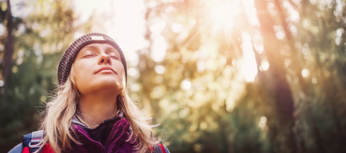 How Does Peripheral Nerve Stimulation Work-7-Nature A woman closes her eyes and smiles in the woods due to peripheral nerve stimulation