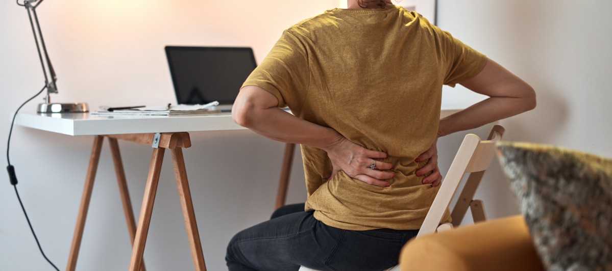Ideal Candidates for Kyphoplasty-2-Pain A woman sitting at a desk grabs her back in pain due to osteoperosis