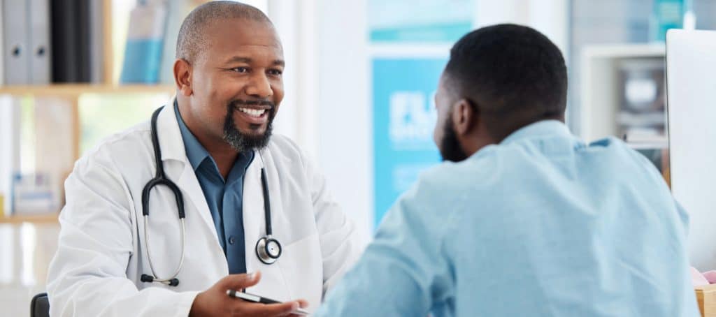 A doctor in a lab coat smiles as he tells a patient about essential amino acid supplements