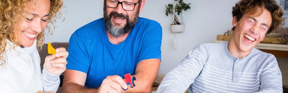 Key Benefits of Trigger Finger Injections-5 A man laughs with his family as they put together a puzzle after his trigger finger treatment